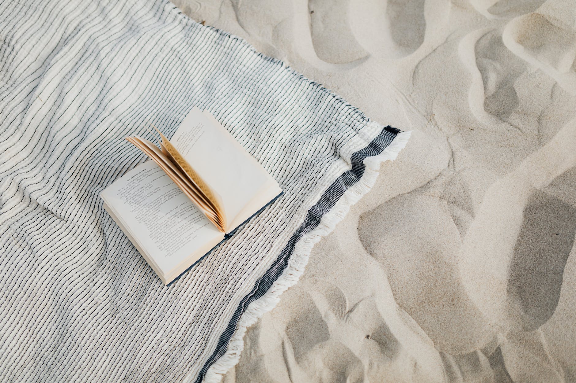 a book on beach towel on white sand